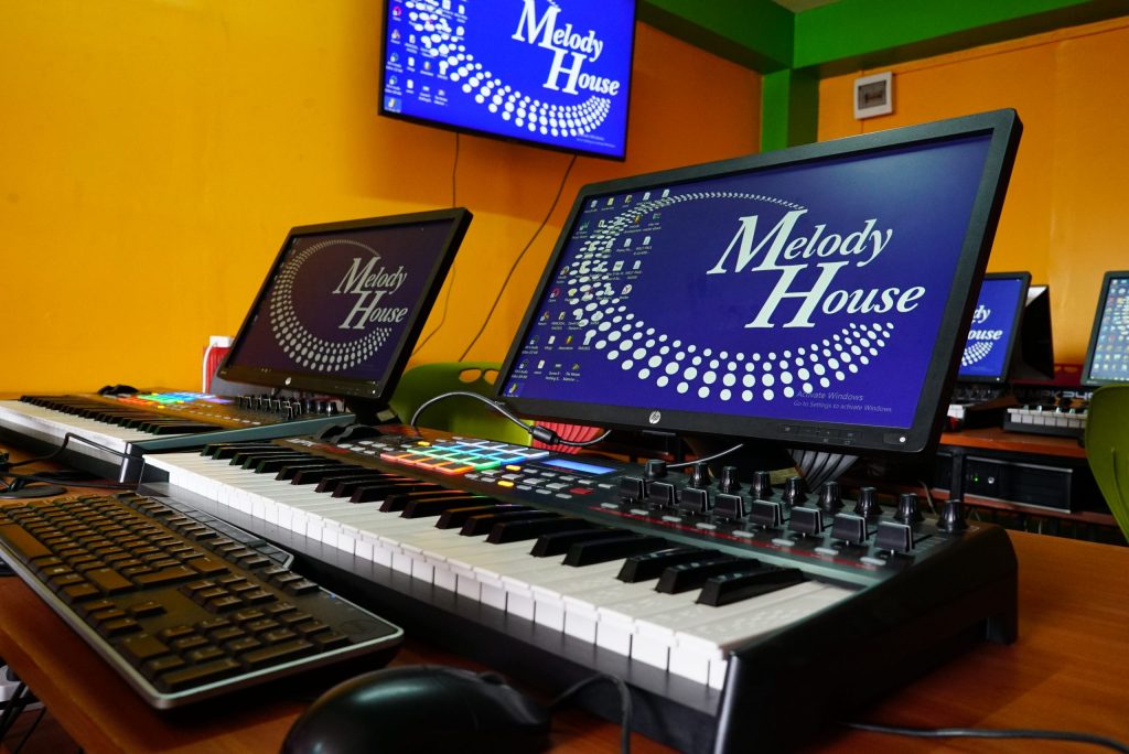 The image features a professional audio setup on a desk, showcasing a MIDI keyboard, studio monitors, and headphones, essential tools for music production. This arrangement represents a hands-on learning experience for students in music production courses, highlighting the importance of quality equipment in the music industry.
