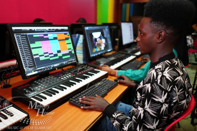 A professional music producer is focused on mixing audio at a sophisticated mixing desk, surrounded by multiple screens that display colorful audio waveforms. This scene highlights the tools and technology essential for sound engineering, showcasing the environment where music production graduates develop their practical skills.